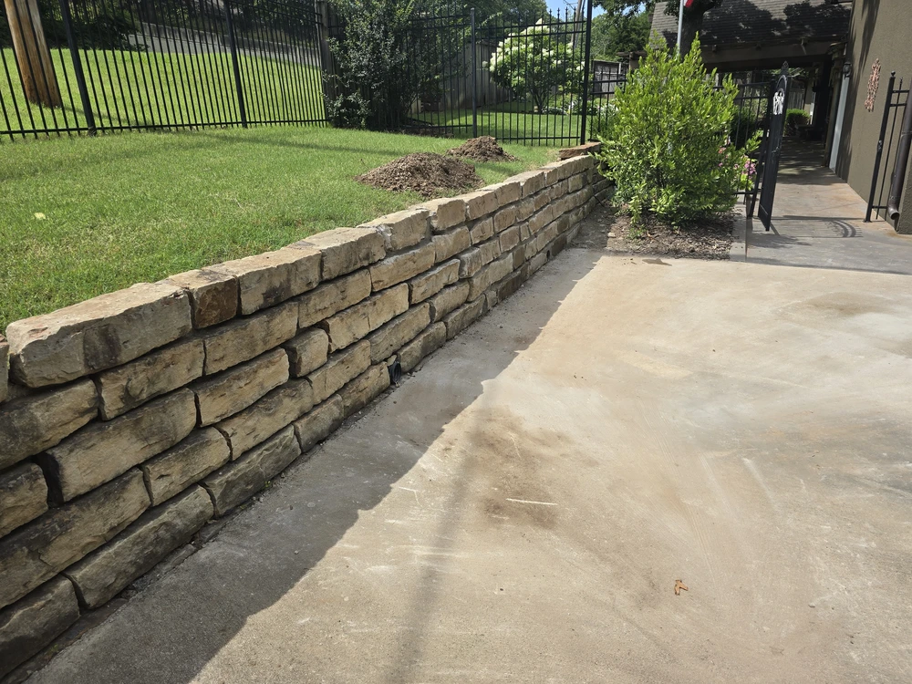 Dark timber retaining wall supporting a raised yard beside a house and green deck.